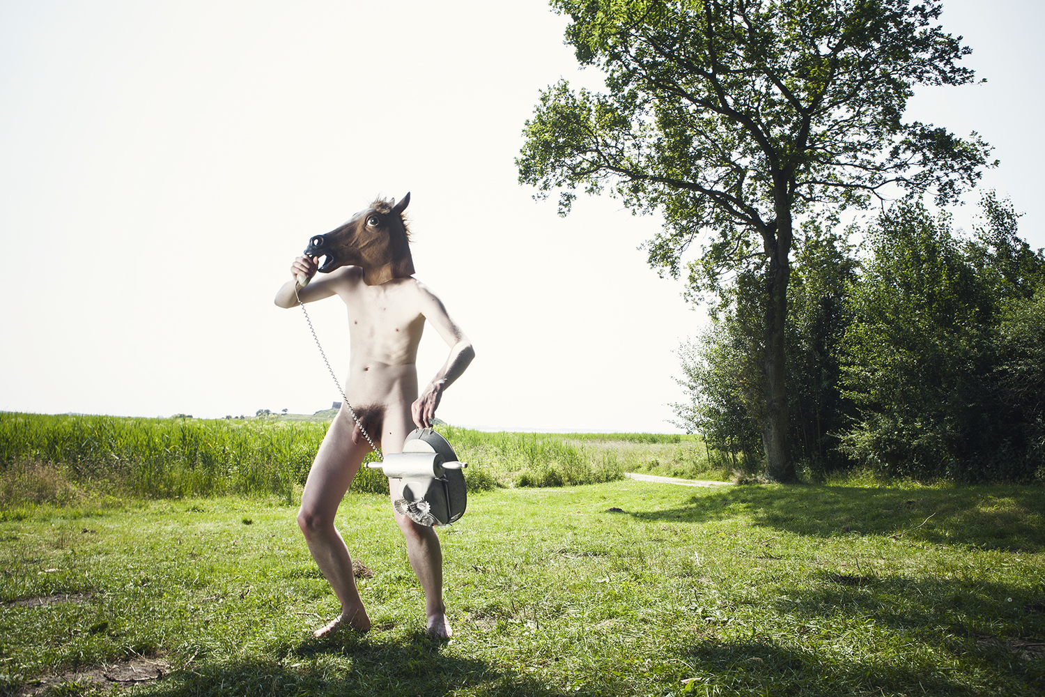 Knaldemand is standing in a small field under a tree, holding a toy rotary phone, calling Dog.